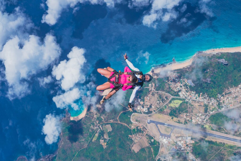 Imagem de salto duplo em Fernando de Noronha durante a queda livre com o arquipélago de fundo e o instrutor atrás da passageira.